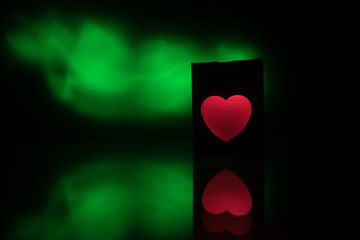Blurred neon heart icon on a dark background. Copy space with red bright colorful heart on black background