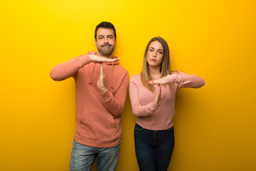 Group of two people on yellow background making stop gesture with her hand to stop an act