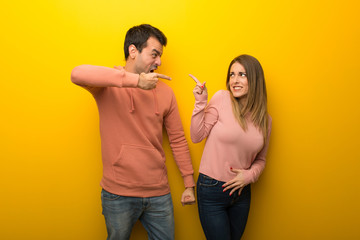 Group of two people on yellow background frustrated by a bad situation and pointing to the front