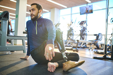 Bearded athlete with amputee leg sitting on the floor and resting in health club