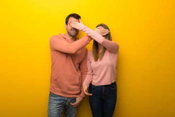 Group of two people on yellow background covering eyes by hands. Surprised to see what is ahead