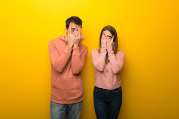 Group of two people on yellow background covering eyes by hands and looking through the fingers