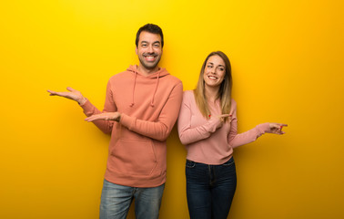 Group of two people on yellow background holding copyspace imaginary on the palm to insert an ad