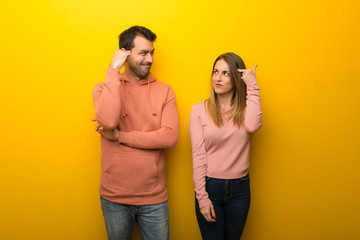 Fototapeta premium Group of two people on yellow background making the gesture of madness putting finger on the head