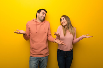 Group of two people on yellow background making unimportant gesture while lifting the shoulders