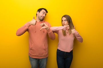 Group of two people on yellow background making good-bad sign. Undecided between yes or not - obrazy, fototapety, plakaty