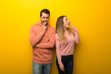 Group of two people on yellow background yawning and covering wide open mouth with hand - obrazy, fototapety, plakaty