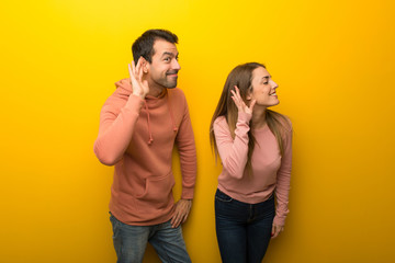 Group of two people on yellow background listening to something by putting hand on the ear