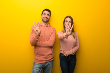 Group of two people on yellow background happy and counting four with fingers