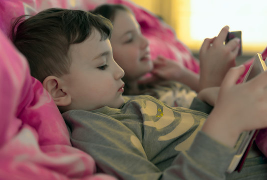 Children in bed playing with gadgets.