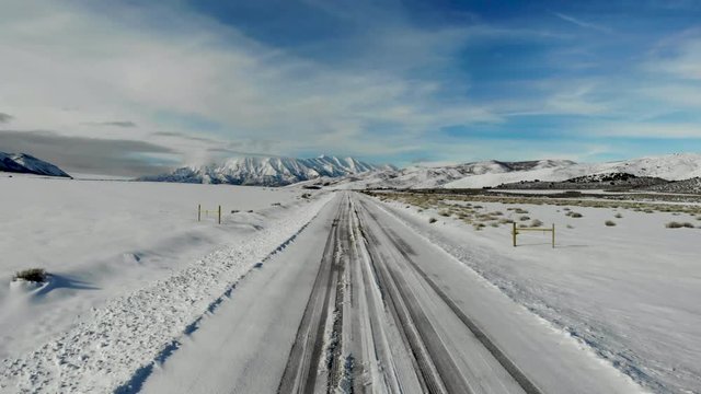 Aerial-Flying slowly over snowy road to vanishing point toward a majestic snow-covered mountain under blue sky with high wispy clouds