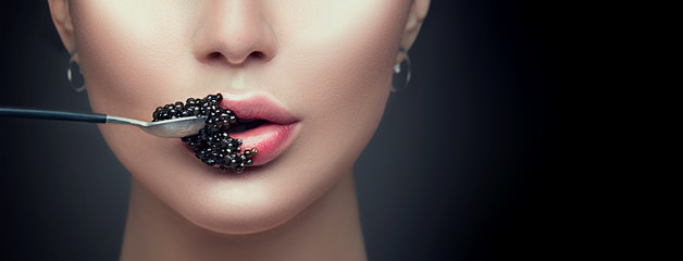Schöne Modelfrau, die schwarzen Kaviar isst. Schönheitsmädchen mit Kaviar auf ihren Lippen lokalisiert auf schwarzem Hintergrund © Subbotina Anna