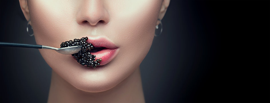 Beautiful fashion model woman eating black caviar. Beauty girl with caviar on her lips isolated on black background