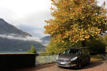 A car parked near tree in autumn colors on the shore of the Como lake with overcast sky as background