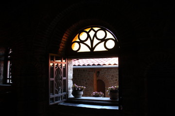 Daylight enters the dark room of the monastery through a small open window with flower pots, wooden frames, thick stone walls, brickwork