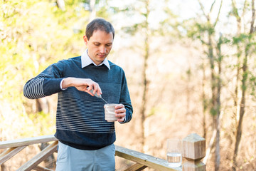 Glass of water and tea cup on wooden railing outside on backyard deck garden and man holding whisk...