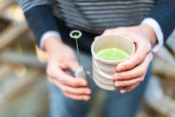 Man holding Japanese tea cup outside on backyard garden with whisk for matcha hot drink and foam