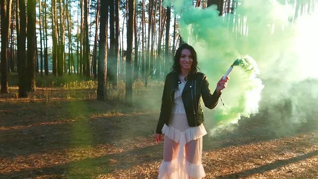 Woman walking in the pine trees forest with colored smoke, sunset, blurred background