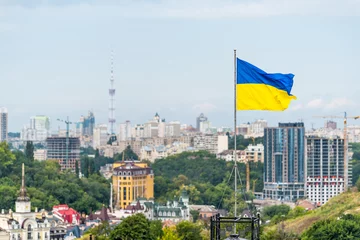 Tuinposter Kyiv, Ukraine Cityscape skyline of Kiev and Ukrainian flag waving in the wind during summer in Podil district © Kristina Blokhin