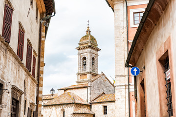 Fototapeta premium San Quirico D'Orcia, Italy Street in town village in Tuscany during sunny summer day and famous church bell tower between alley
