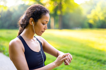 Sport asian woman listening to music with headphones while looking at watch outdoors