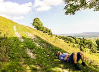 One man wearing a blue t shirt, laying down and resting under a tree on a hill. Taken on a sunny summer day on the Hesselberg mountain in Middle Franconia, Germany
