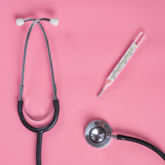 Mercury thermometer and stethoscope on a pink background