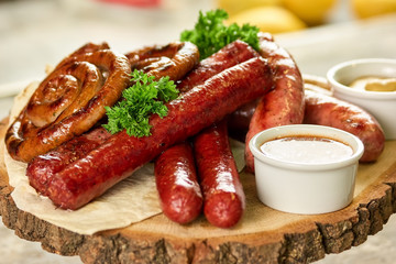 Assorted grilled sausages with sauce on rustic round wooden board. Smoked grilled sausages with sauce on lavash.
