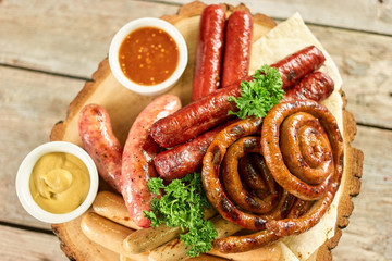 Down view on sausage assortmet with garnish. Coil sausages, wieners, frankfurters, sauces, parsley, lavash and wooden plate, top view.