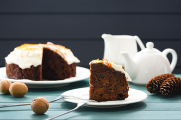 Hygge dessert. Chocolate fruit cake with cream cheese icing and orange peel decorated with nuts and cones on blue background copyspace