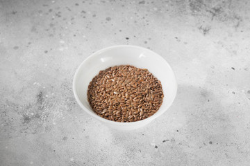 Flax seeds in a white bowl on a gray kitchen table. Organic health food