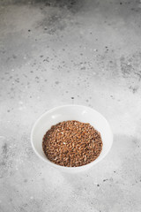 Flax seeds in a white bowl on a gray kitchen table. Organic health food