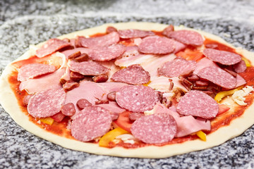 Uncooked pizza with sliced salami, ham and sausages. Pizza is ready to be baked.