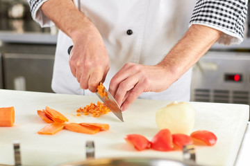 Chef chopping carrot. Cooker man chopping carrot on kitchen board.