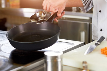 Chef greasing pan with oil. Cooker man pouring oil on pan from metal sauce boat. Preparation for frying.