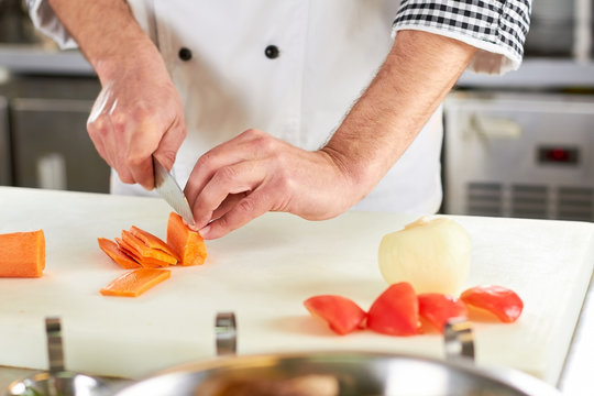 Man Use Knife To Slice Carrot. Chef Preparing Some Carrots On A Cutting Board For Cooking.