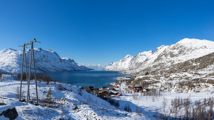 Sunny winter daytime view on Erstfjordbotn, Kvaloya, Tromso, Norway with fjord, sea, mountains and snow