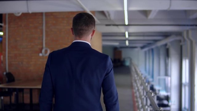 Back View Businessman Wearing Blue Suit Walking In Loft Office Slow Motion. Manager At Work