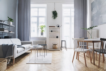Bright home nordic living room with design sofa, family table, plant, white bookstand on the wall. Brown wooden parquet. Abstract painting on the white wall.  Concept of minimalistic interior. - obrazy, fototapety, plakaty