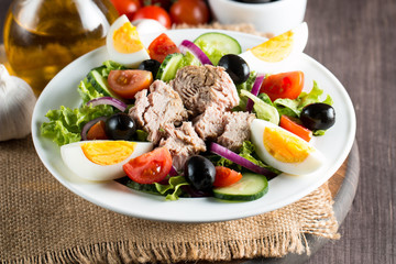 Fresh fish tuna salad made of tomato, ruccola, tuna, eggs, arugula, crackers and spices. Caesar salad in a white bowl on wooden background
