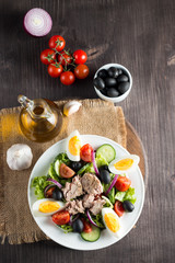 Fresh fish tuna salad made of tomato, ruccola, tuna, eggs, arugula, crackers and spices. Caesar salad in a white bowl on wooden background