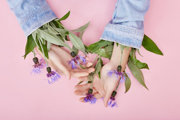 Hands and spring flowers are on a pink table skincare. Nature Cosmetics for hand skin care, a means to reduce wrinkles on hands, moisturizing. Natural cosmetics from flower extract, beauty and fashion