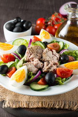 Fresh fish tuna salad made of tomato, ruccola, tuna, eggs, arugula, crackers and spices. Caesar salad in a white bowl on wooden background