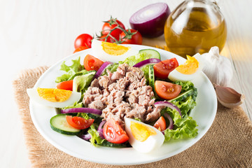 Fresh fish tuna salad made of tomato, ruccola, tuna, eggs, arugula, crackers and spices. Caesar salad in a white bowl on wooden background