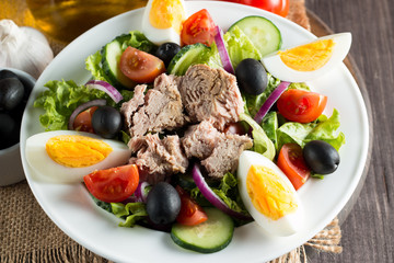 Fresh fish tuna salad made of tomato, ruccola, tuna, eggs, arugula, crackers and spices. Caesar salad in a white bowl on wooden background
