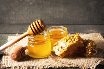 Honey dripping from a wooden honey dipper in a jar on wooden grey rustic background