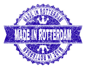 MADE IN ROTTERDAM rosette seal watermark with grunge effect. Designed with round rosette, ribbon and small crowns. Blue vector rubber watermark of MADE IN ROTTERDAM caption with corroded texture.