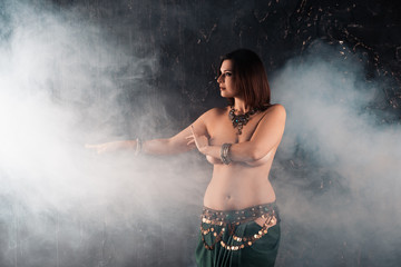 Sexy women performs belly dance in ethnic dress on dark smoky background