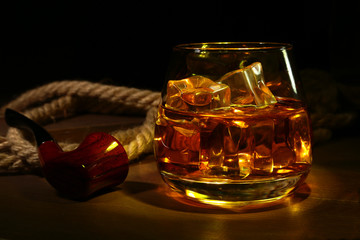 Whiskey, cognac or brandy with ice in glasses and smoking pipe on rustic wood background, copy space.
