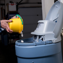 Yellow bucket pours salt pellets by a man into a water softener
